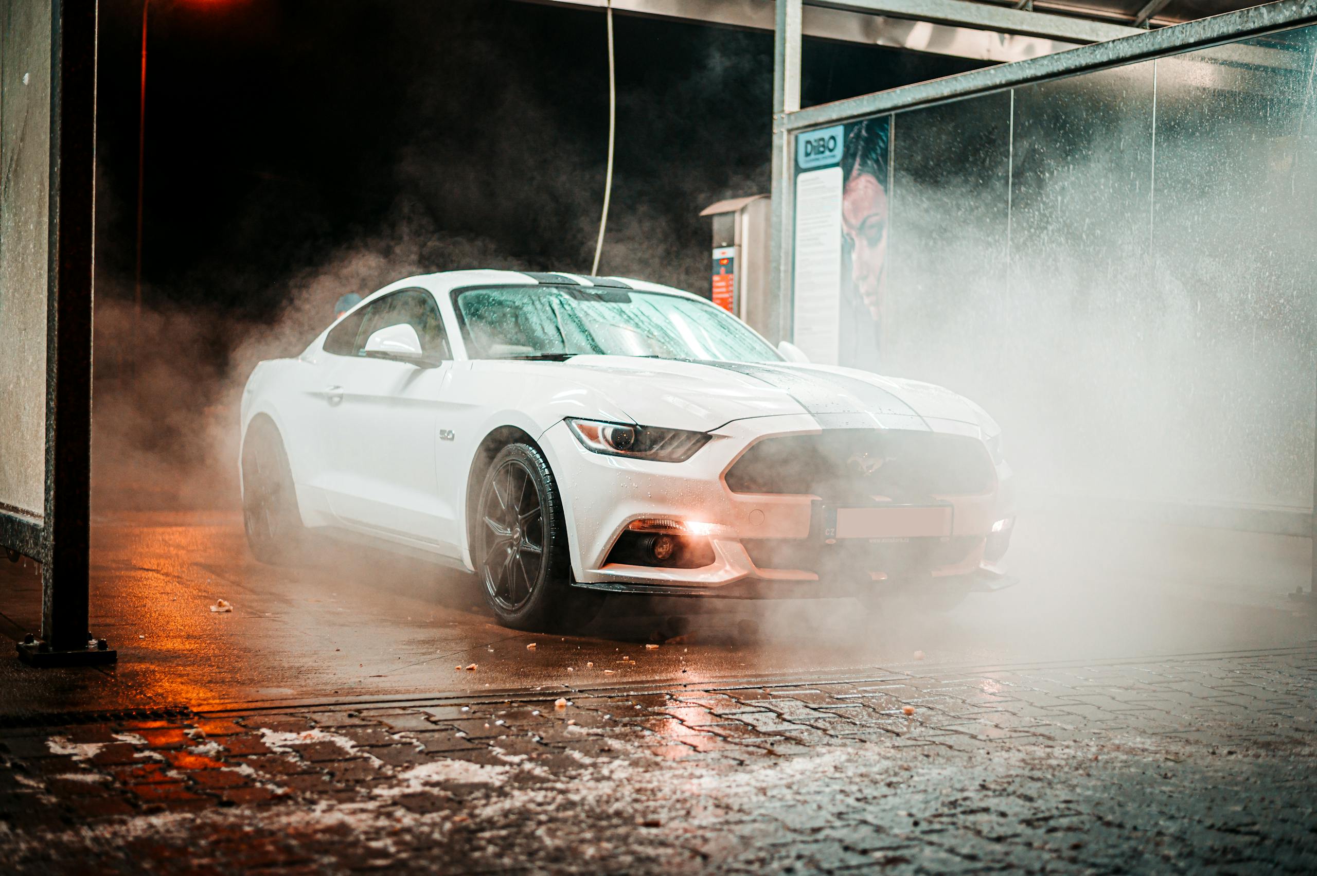 About Us White Ford Mustang in a misty carwash setting, illuminated at night in an urban environment.