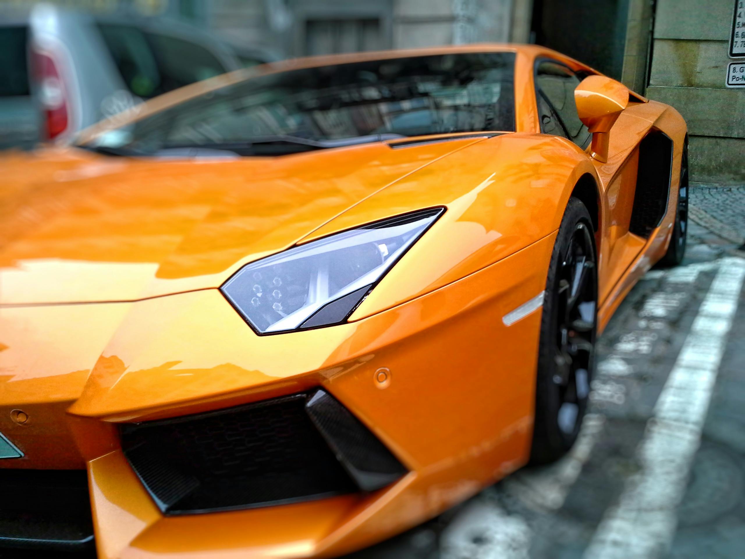 About Us A striking orange luxury sports car parked on a city street in Brno, Czechia.